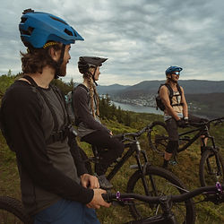 Drei Personen auf Mountainbikes mit Blick auf einen Fjord.