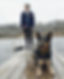 Assistant Sara is standing on a dock with her blue heeler in a down stay.