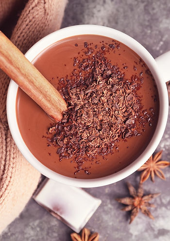 Cup of rich hot chocolate topped with grated dark chocolate and cinnamon stick, served with cozy textures and star anise for a warming winter drink.