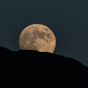 Full Buck Moon rising above a dark mountain ridge against a deep blue twilight sky, symbolizing strength, growth, and spiritual reflection.