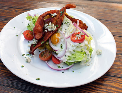 Bacon Wedge. Large portion of iceberg lettuce topped with blue cheese dressing, baby heirloom tomatoes, red onions, blue cheese crumbles, and two thick slices of applewood bacon.