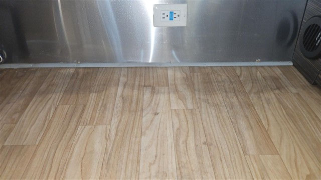 Empty room with wood-look floor and stainless steel wall, a centered electrical outlet, and a dark vented speaker on the right.