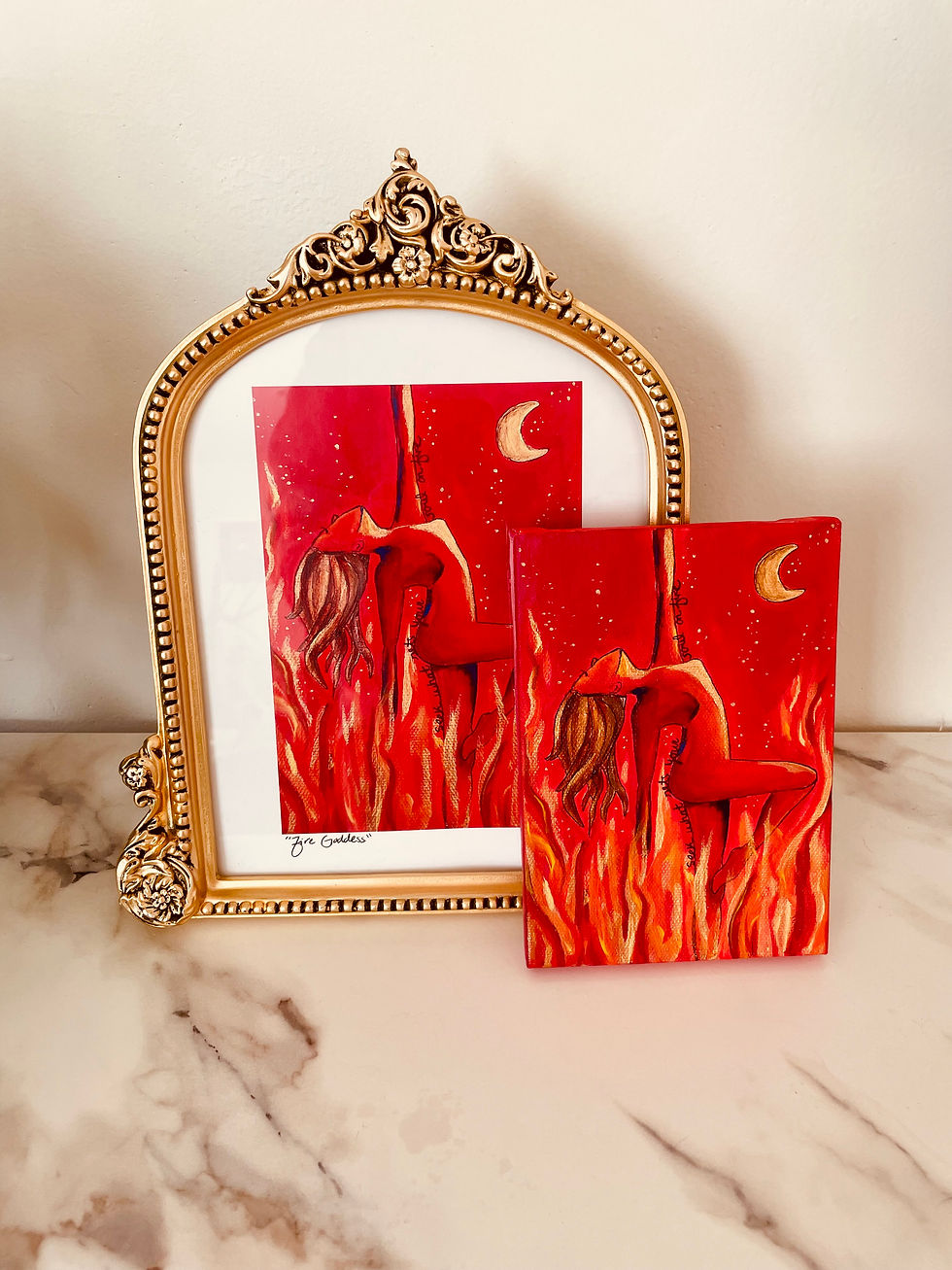 Thumbnail: The print of the Fire Goddess next to the original painting. She is red with auburn and bronze hair. She is dancing in flames and there are gold sparks reaching for a crescent moon. 