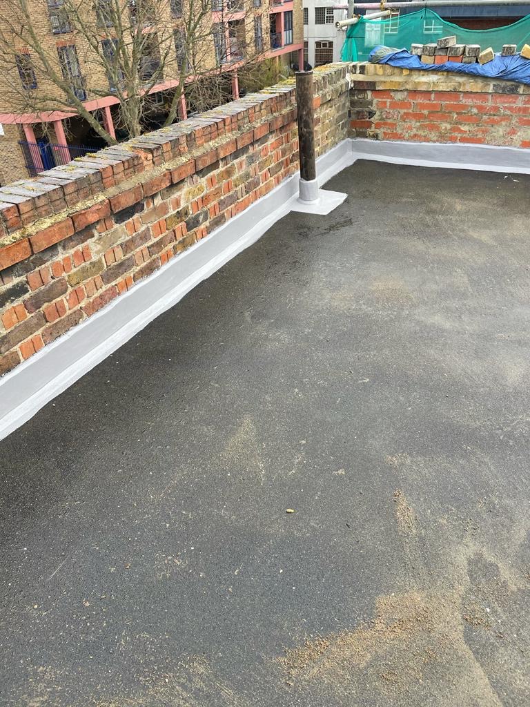 The image shows a waterproof falt roof close-up view of a newly installed flat roof made of grey material, with a clean and well-maintained appearance. The roof features white flashing at the edges.