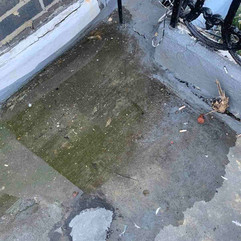 Damaged concrete floor with cracks, water stains, and exposed wires near a brick wall.