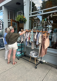 Customers shopping a clothing rack on display in front of Owen + Sage - click for shopping directory