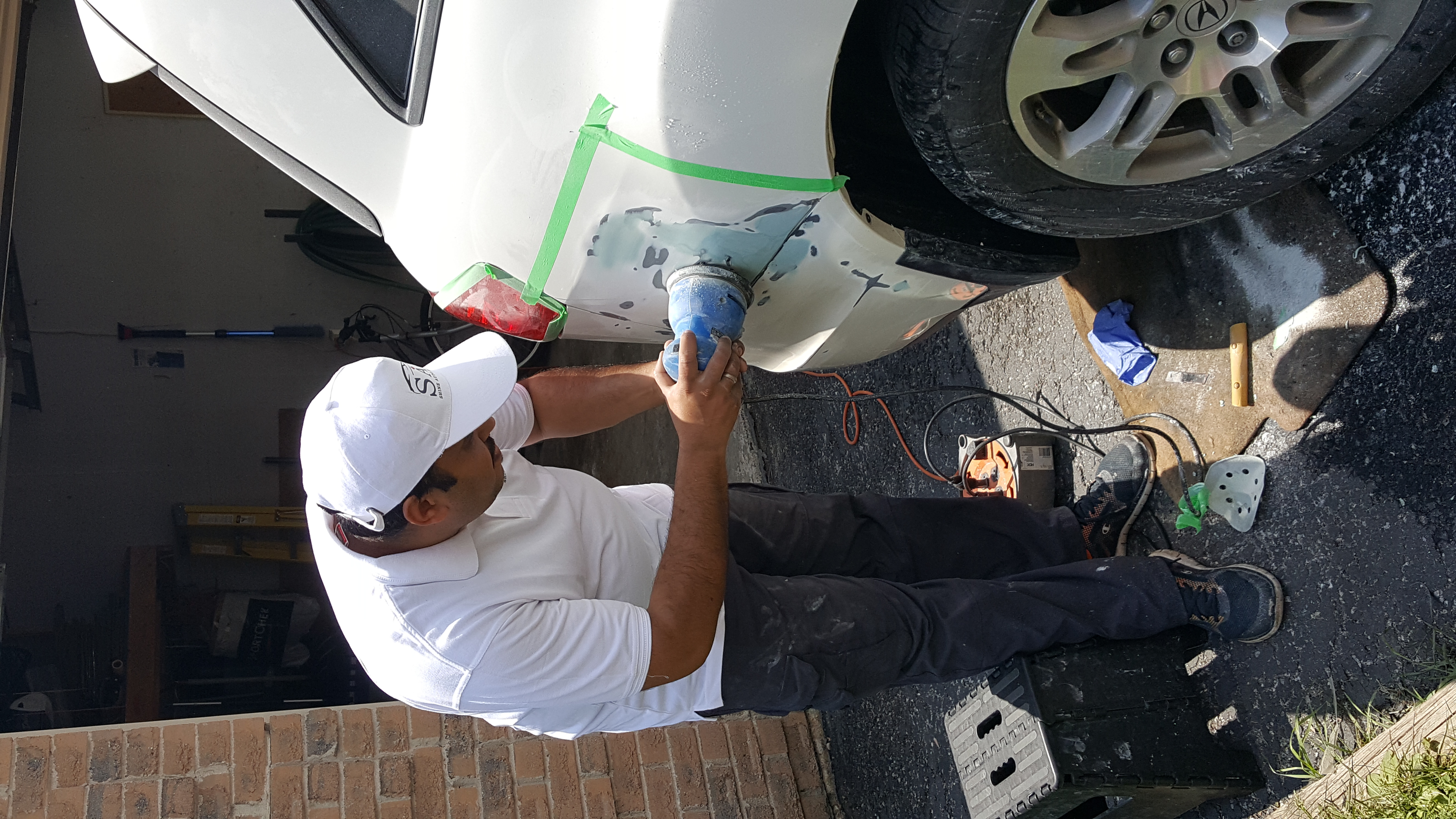 Wahid sanding a masked white SUV panel during bodywork preparation