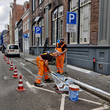 Two construction workers adding streetmarking with a template and paint on a street in Groningen