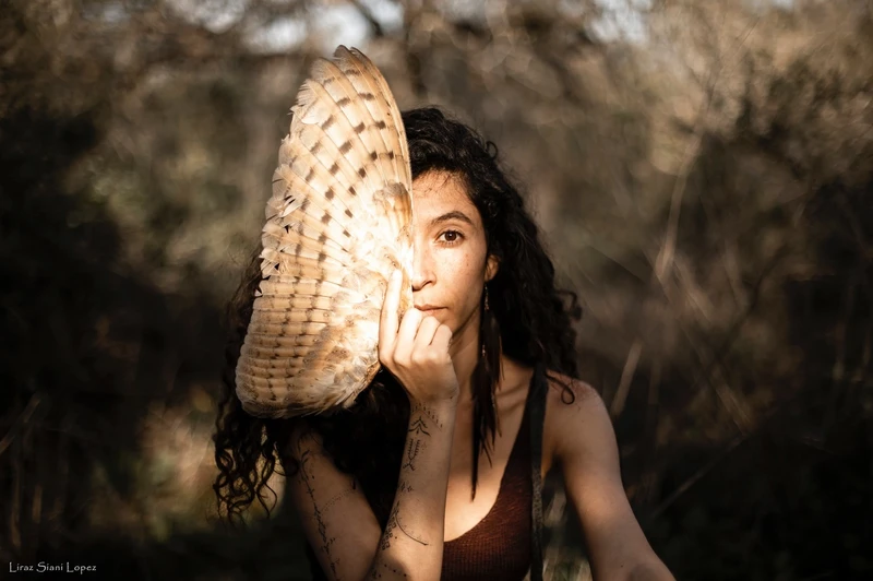 Woman partially hides face with feathers, outdoor setting