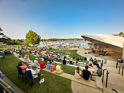 Bandshell with a marina in the background and a crowd in the foreground enjoying a live music performance.