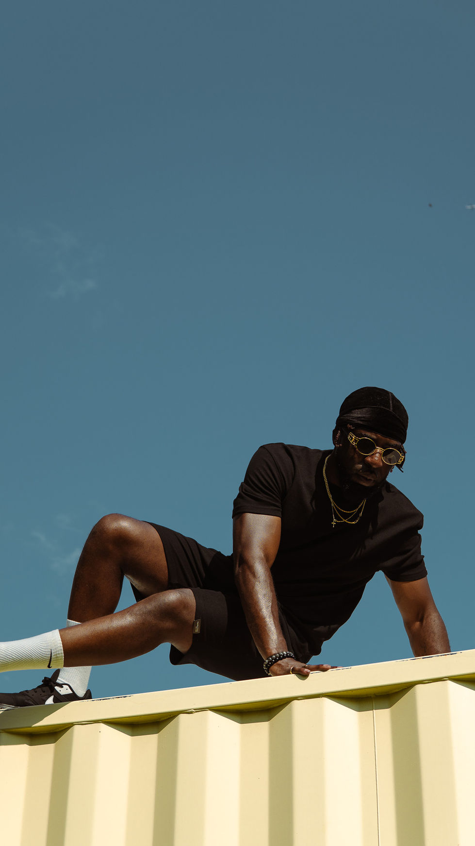 Man in black outfit sitting against blue sky.