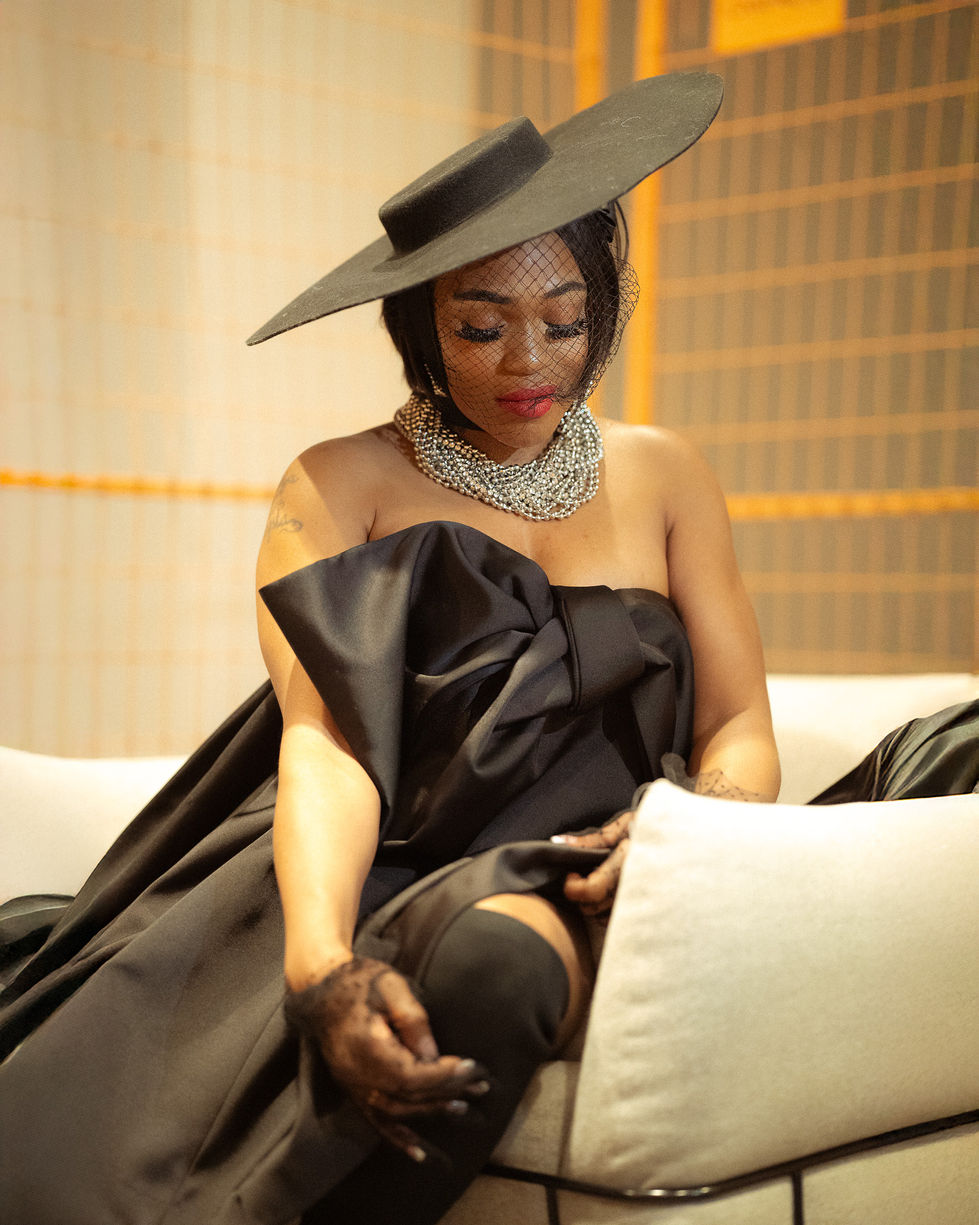 Woman in elegant black dress and hat, sitting indoors.