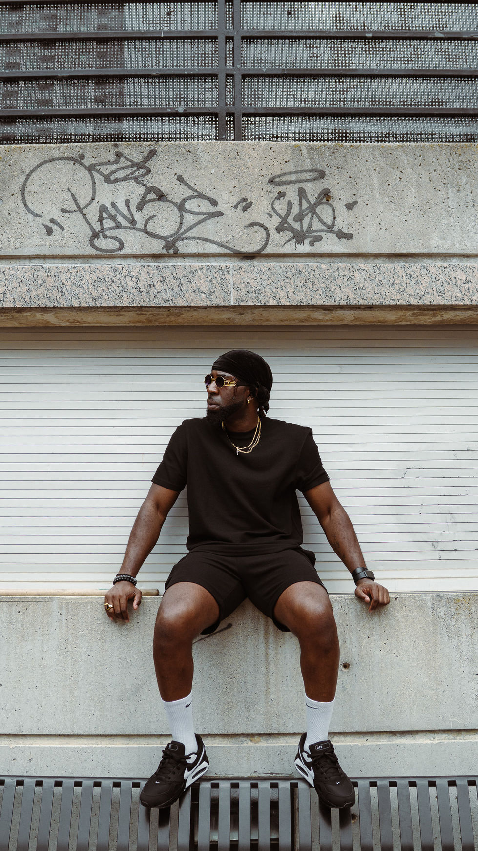 Person in black outfit sitting against graffiti wall.