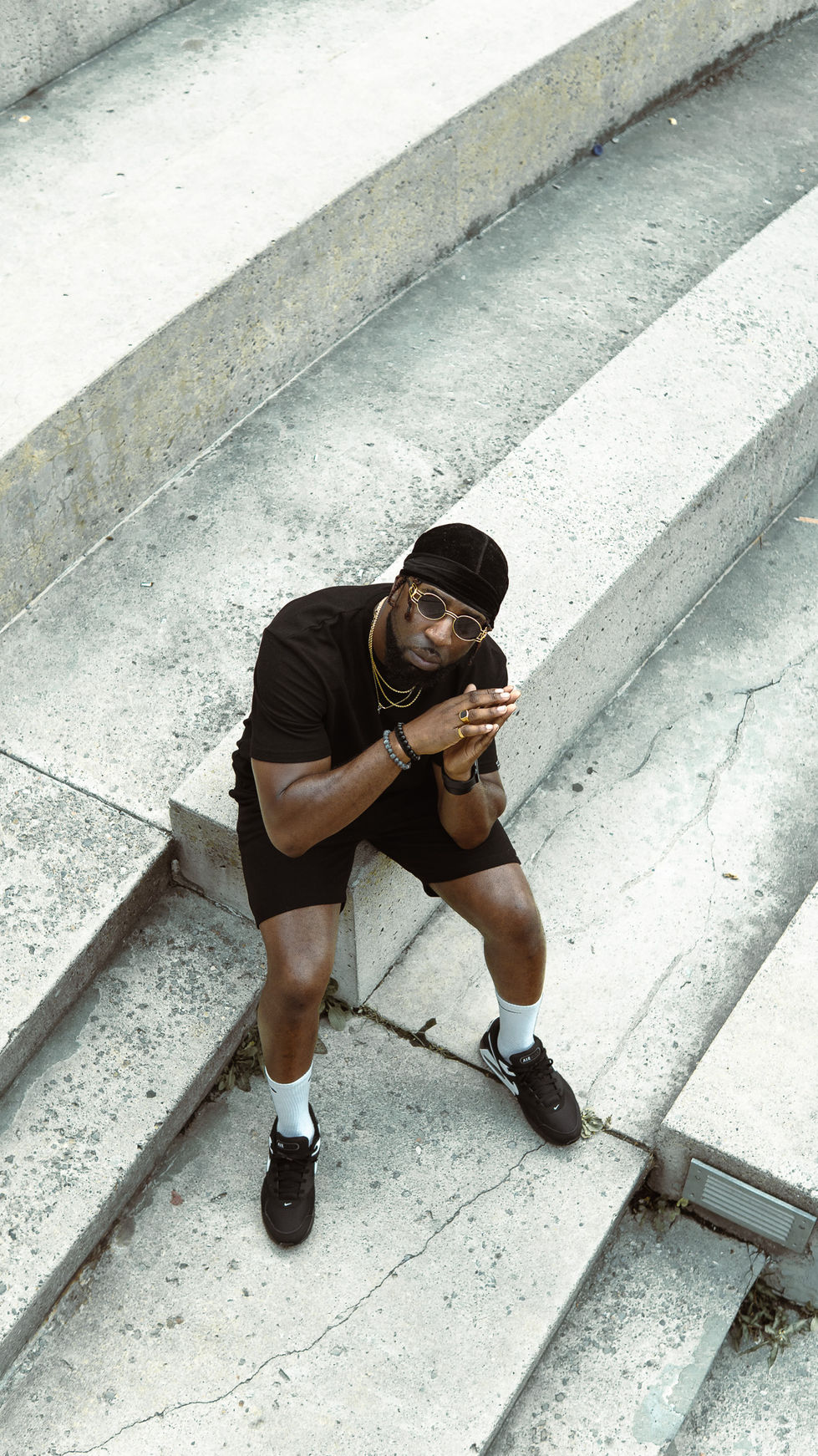Person sitting on steps, wearing black outfit and sunglasses.