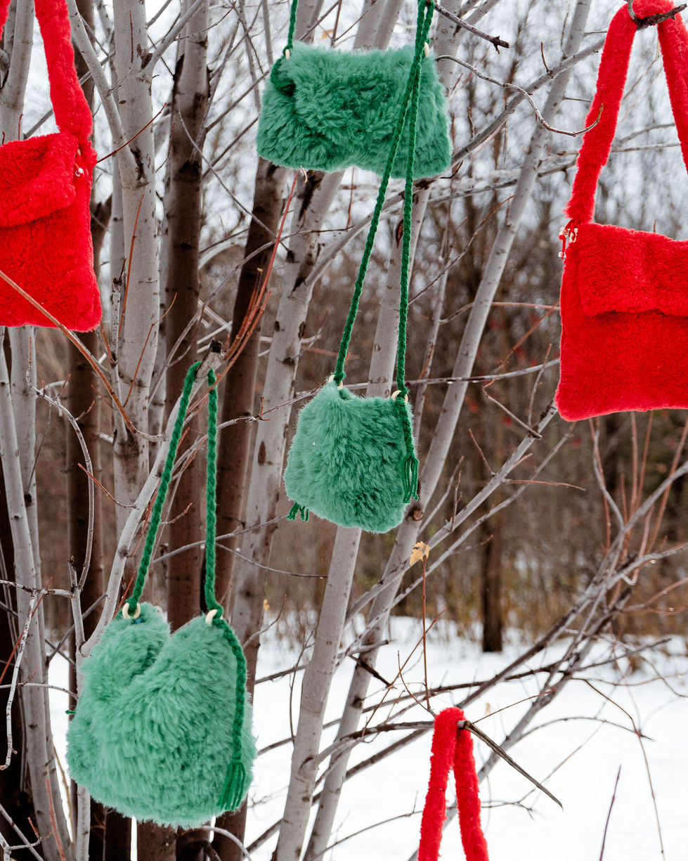 Colorful fuzzy bags hanging on tree branches in snow.