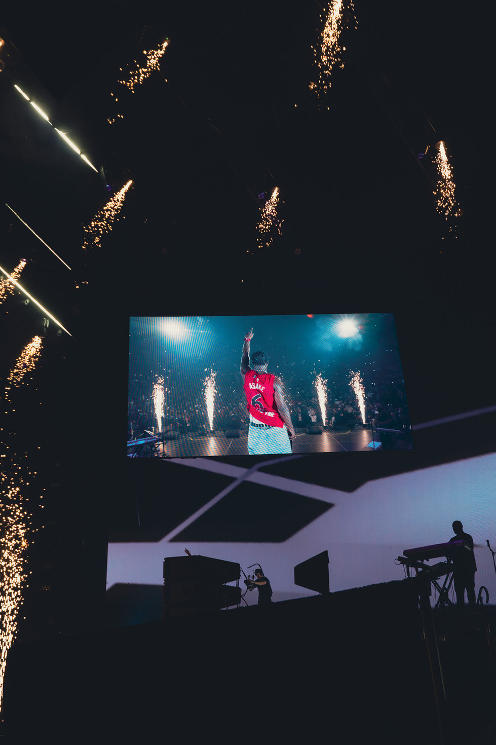 Performer on stage with fireworks and large screen.