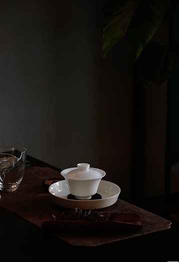 Vit kinesisk gaiwan och glas på tebricka i mörk miljö – symbol för gongfu-te och teceremoniens estetik