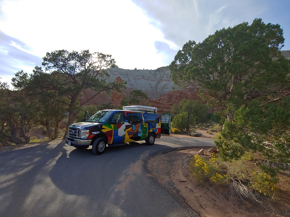Camper van parked at a campsite among juniper trees and sandstone cliffs.