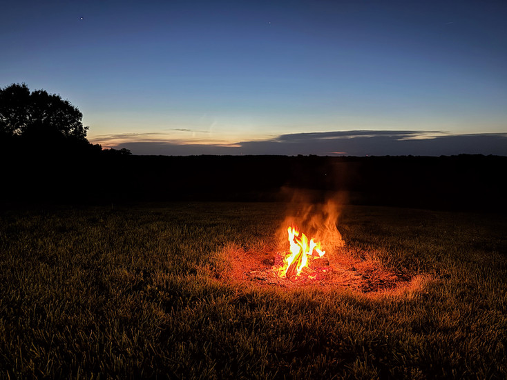 A backyard campfire, right after dusk, with one lone star shining in the sky.