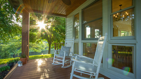 A rural home, with beautiful covered front porch, adorned with a pair of white rocking chairs.