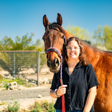 Gwen with her horse standing in front of a fence and some palm trees.