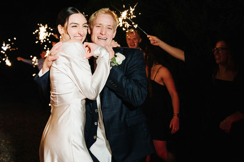 A newlywed couple exits their wedding to guests waving and holding sparklers. 