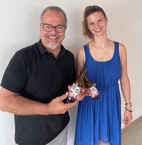 Moderator Fredi Fritz mit Hey Sis. Beide halten eine Hey Sis Bierflasche in der Hand und stoßen dabei an.