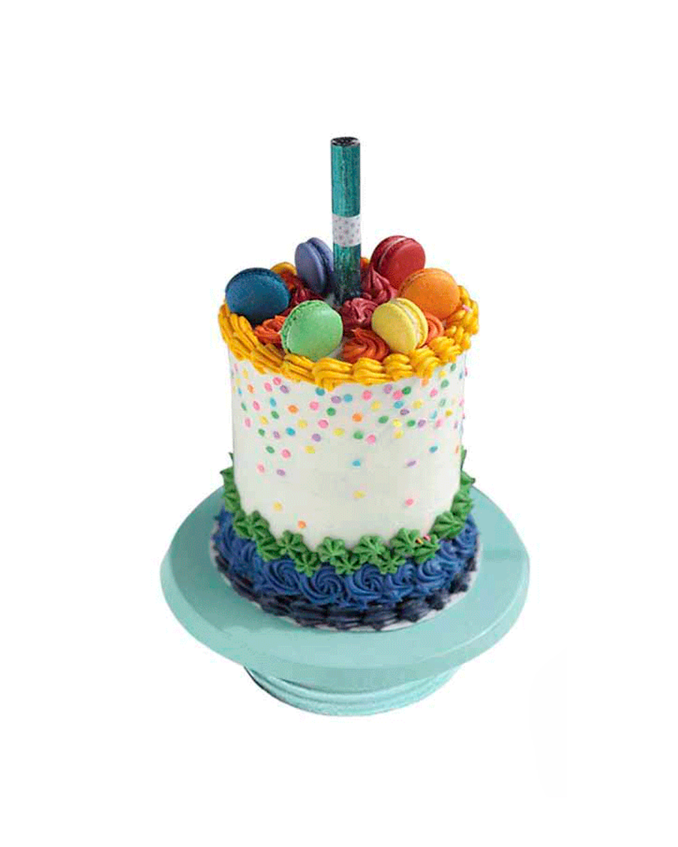 Pastel de Pride blanco con detalles de confetti y bordes en buttercream de colores, coronado con macarons