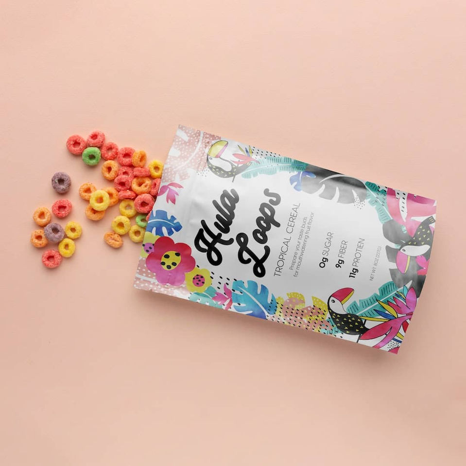 Hula Loops tropical cereal packaging design with colorful floral and toucan patterns, showcasing a healthy cereal with 0g sugar, 9g fiber, and 11g protein.