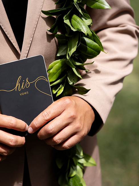 Hands holding 'his vows' notebook, green lei in Hawaii