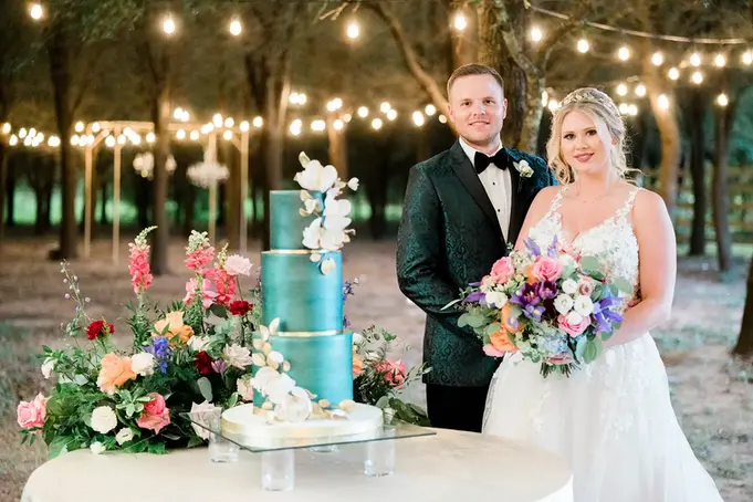 Bride and groom outdoor portrait next to their emerald green cake with colorful flowers at A Thousand Oaks Events & Retreats in Cypress, TX