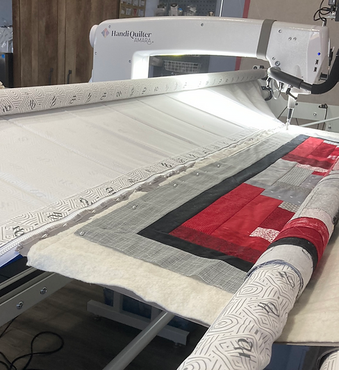 Handi-quilter Amara long arm quilting machine and frame with red, gey and black quilt loaded.