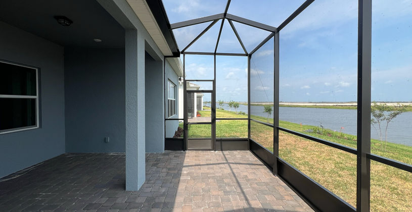 Screened-in patio with pavers overlooking a lake.