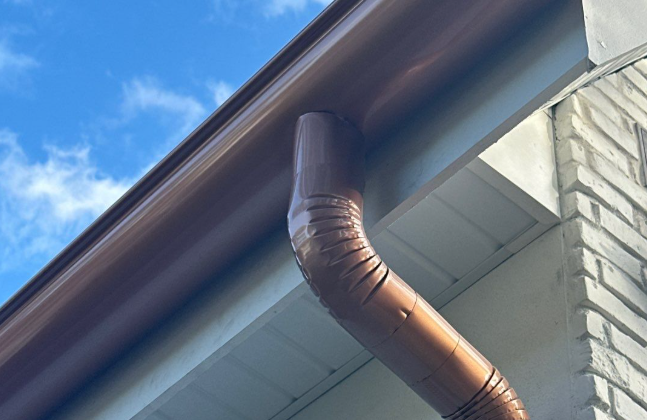 Brown rain gutter and downspout on a white brick house