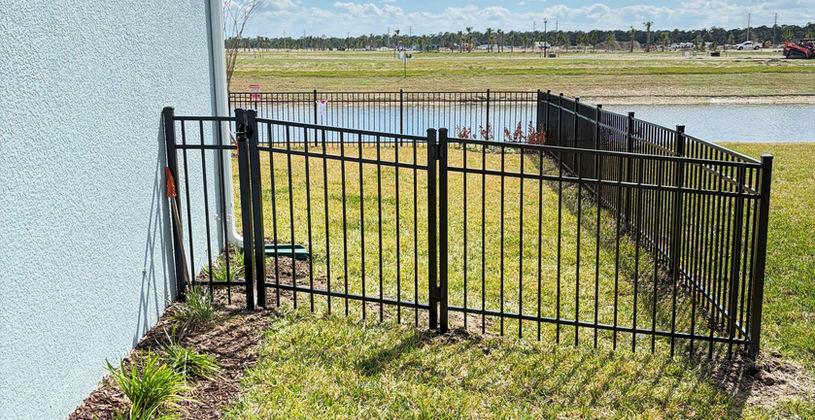 Black aluminum fence bordering a backyard lawn and pond