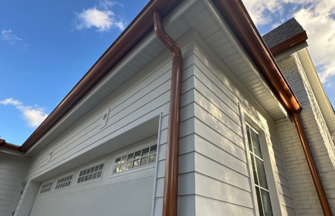 Copper gutters on white siding corner with garage