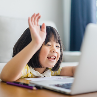 Child sitting infront of a laptop smiling with the right hand raised up.