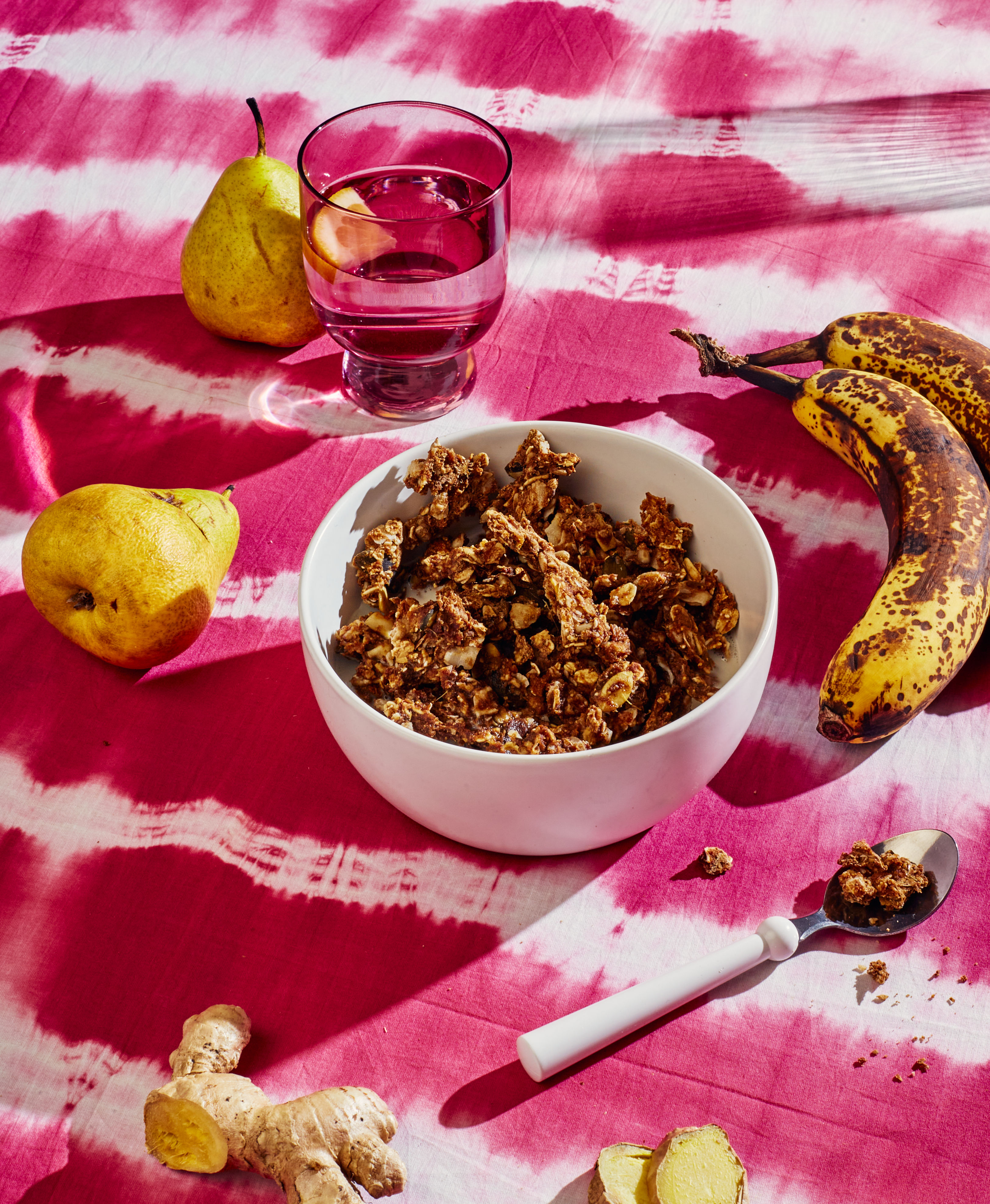 A bowl full of Bruized Ginger Spice Pulp Crunch granola, surrounded by spotty bananas and imperfect pears.
