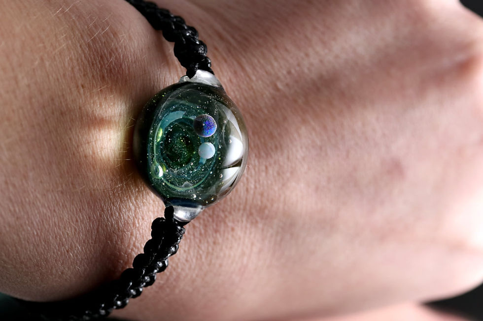 Thumbnail: Bracelet galaxie avec une voie lactée  de couleur verte et bleu avec deux planète en apesanteur.
le bracelet galaxie est  porté sur un poignet d'homme
