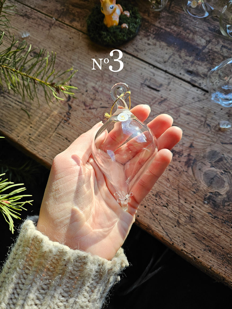 Main tenant a glass object. Text "N°3". Boule de Noël en verre soufflée. Still life.