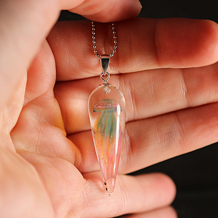 Collier méduse translucide de couleur verte et rose qui est posé sur une mains.