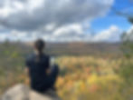 Personne assise de dos sur un rocher, observant un paysage d’automne coloré avec des arbres rouges, jaunes et orangés, au Québec.