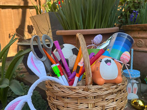a basket full of random items like balls, pens, scissors, cups, easter eggs and bunny ears.