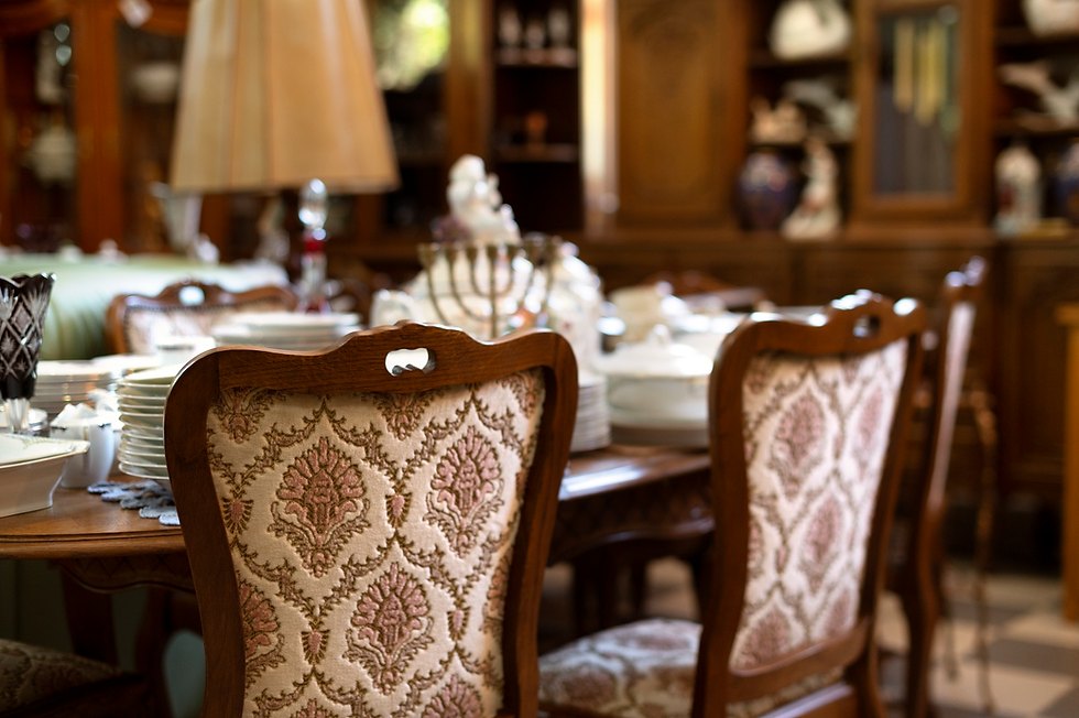 Elegant dining room with ornate wooden chairs featuring floral upholstery around a table set with fine china. Shelves in blurred background.