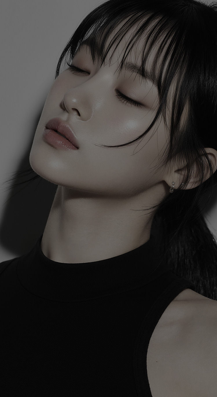 A woman with black hair wearing a black top, standing against a neutral background.