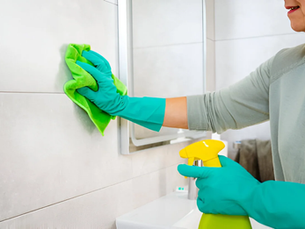 Close up of woman's hands cleaning bathroom tiles with a microfiber cloth and spray cleaner