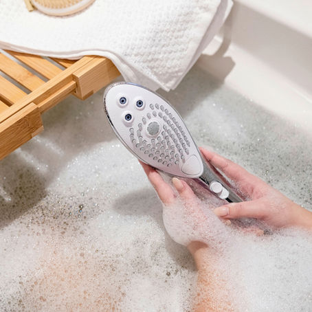 Womanizer Wave gehalten von Frauenhand in schaumbedeckter Badewanne
