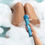 Miniaturbild: hellblauer Massagestab von le Wand. gehalten von einer Frauenhand in einer schaumbedeckten Wanne. nackte Beine sichtbar
