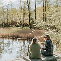 Jenny sitting on a log beside a body of water, talking to a client.