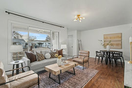Staged small Old Colorado home featuring low-profile gray sofa, accent chairs, neutral rug, clear base lamps, compact dining table with oversized wall art, and teal accent pillows tying in kitchen cabinetry